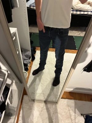 Mörkblå slim fit jeans herr - Säljer ett par mörkblå slim fit jeans med klassisk femficksdesign och normal midja. Jeansen har smal passform hela vägen ner och är tillverkade i ett stretchigt denimtyg för extra komfort. Perfekta till en avslappnad stil.