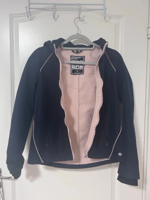 Svart vindjacka med rosa fleece - svart vindjacka med ljusrosa fleecefoder. Jackan har huva, dragkedja och framtill 