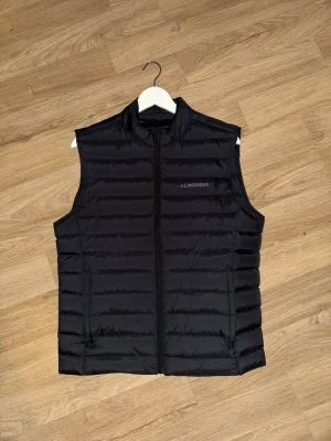 Svart dunväst från J.Lindeberg -  Säljer en väst från J-Lindberg i storlek M.  Färgen är svart och den  är knappt använd och i mycket fint skick.