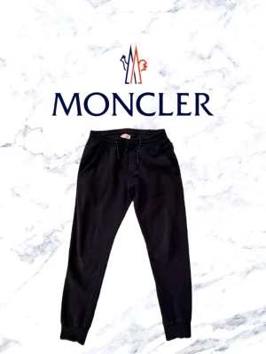 Svarta mjukisbyxor från Moncler - Säljer ett par svarta mjukisbyxor från Moncler med muddar vid bensluten. Byxorna har två sidofickor och är gjorda i mjukt bomullsmaterial. Perfekta för chill dagar eller när du vill vara bekväm. Kan paras ihop med en simpel vit t shirt för en avslappnad look