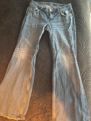 Blå bootcut jeans  - Säljer ett par ljusblå bootcut jeans. De har fått slitningar längst ner på benen. Jeansen har klassisk femficksmodell och knappgylf. Perfekta för dig som gillar en avslappnad och trendig look.
