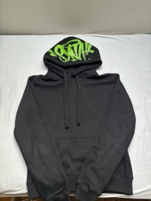 Svart hoodie med grön graffiti-huva - Säljer en svart hoodie med huva och snören. Insidan av huvan har en cool grön graffiti-text som sticker ut. Hoodien har ribbade muddar vid ärmar och midja samt en klassisk känguruficka framtill. Perfekt för dig som gillar streetwear och vill ha något unikt. Strlk M 