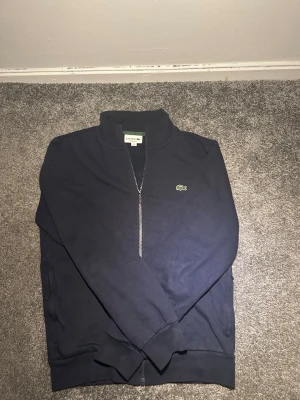 Marinblå ziptröja från Lacoste - Marinblå full zip/kofta från Lacoste. Mycket bra skick. Storlek S. Äkta tröja från Lacoste. 