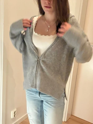 Grå ziphoodie med huva - Mysig grå ziphoodie med huva och dragkedja framtill. Tröjan har långa ärmar, ribbade muddar och slitsar i sidorna. Perfekt för lager-på-lager och chill dagar. Enkel och stilren design som passar till det mesta.