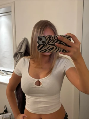 Vit ribbad croppad topp  - Säljer en vit ribbad croppad topp med korta ärmar och snygg nyckelhålsdetalj framtill. Perfekt för dig som gillar trendiga och stilrena plagg. Passformen är tight och materialet känns mjukt mot huden.