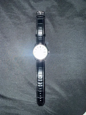 Seiko klocka med svart läderarmband - Stilren Seiko klocka med vit urtavla och svart läderarmband med krokodilpräglad yta. Klockan har silverfärgade detaljer, datumvisning och är vattentät upp till 100 meter. Perfekt accessoar för dig som gillar klassisk och tidlös design.