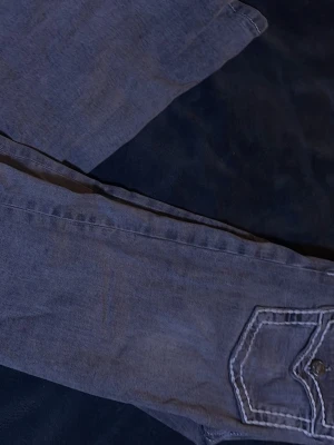 Gråa jeans med kontrastsömmar - Säljer ett par gråa jeans med raka ben och tydliga vita kontrastsömmar på bakfickorna. Jeansen har två bakfickor med lock och knappdetaljer.💕