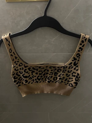 Leopardmönstrad ribbad linnetopp - Snygg ribbad linnetopp i beige med svart leopardmönster. Toppen har breda axelband och är croppad i modellen. Perfekt att styla till högmidjade jeans/konstumbyxor. 