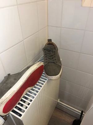 Christian Louboutin grå mocka sneakers - Säljer ett par gråa sneakers från Christian Louboutin med klassisk röd sula. Skorna är i mocka med rund tå, snörning och vit platt sula. Insidan är beige och de kommer med original dustbag. Perfekt för dig som gillar stilrena och lyxiga sneakers.