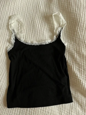 Svart linne med spets - Snygg svart linne med vita spetsdetaljer längs axelbanden och urringningen. 