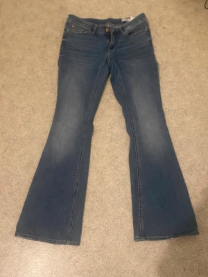 Blå bootcut jeans med utsvängda ben - Säljer ett par klassiska blå bootcut jeans med utsvängda ben och femficksmodell. Jeansen har en snygg tvätt med lätt slitning framtill och normal midja. Jeansen är väldigt streachiga. Perfekta för dig som gillar retrostil och vill ha ett par jeans som sticker ut lite extra.