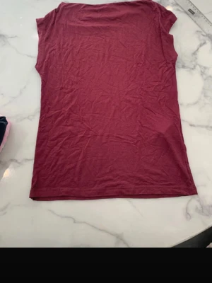 Vinröd enkel t-shirt - Säljer en vinröd t-shirt i mjukt och tunt material. T-shirten har korta ärmar och rak passform, perfekt för en avslappnad stil. Inga synliga tryck eller detaljer, bara en clean och basic look.