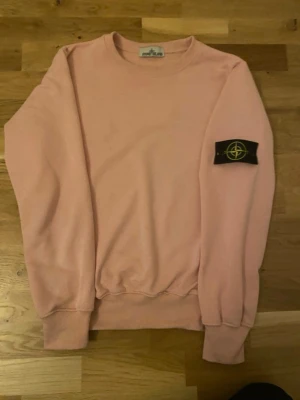 Ljusrosa sweatshirt från Stone I - Säljer en ljusrosa sweatshirt från Stone I med klassisk logotyp-patch på vänster ärm. Tröjan har rund halsringning, ribbade muddar och är tillverkad i mjukt bomullsmaterial. Perfekt för en avslappnad och trendig stil.