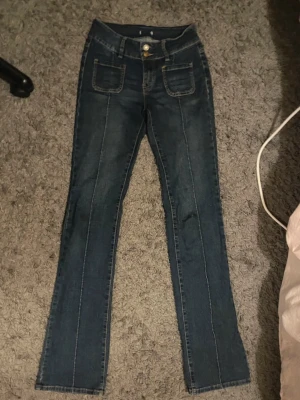 mörkblå bootcuts madlady - Snygga mörkblå bootcut-jeans från Madlady med fickor baktill och en superfin passform. 💕Perfekta för dig som är längre, då modellen är TALL och sitter riktigt bra på långa ben💌  ❣️Bootcut-modell ❣️ Mörkblå färg – lätt att matcha ❣️ Fickor baktill ❣️Storlek 34, TALL  ⚠️ Finns slitningar längst ner på benen, men inget som påverkar användningen – i övrigt är jeansen i bra skick och fortfarande mycket snygga.Innerbenslängden 90 cm & midjemått 32 cm💕