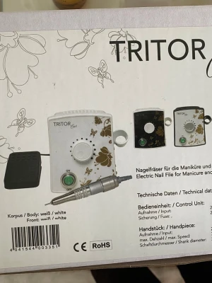 Tritor Elite elektrisk nagelfil - Elektrisk nagelfil från Tritor Elite i vitt med guldfärgade fjärilar och blommor. Kommer med kontrollenhet, handstycke och fotpedal. Perfekt för manikyr och pedikyr. Materialet är plast och metall, och designen är modern och stilren.