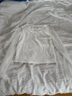 Vit blus med blommspets - Söt vit blus med tyg armar och små prickar.🤍 Blusen har fina spetsdetaljer och blommor vid halsringningen.🌸 Perfekt för dig som gillar classy men också uppklätt.🎉Materialet känns lätt och luftigt.💓🤍