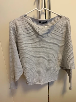 Ljusgrå ribbad tröja från Ginatricot - Säljer en ljusgrå ribbad tröja från Ginatricot med bred halsringning och avslappnad passform. Tröjan har långa ärmar och är tillverkad i ett mjukt, stretchigt material. Perfekt för en chill och stilren look.