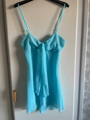 Ljusblå längre topp med knyt - Söt ljusblå längre topp med tunna axelband och knyt framtill. Toppen har en lätt utsvängd passform och är tillverkad i ett tunt, luftigt material som ger en flowy känsla. Perfekt för varma dagar och somriga tillfällen.