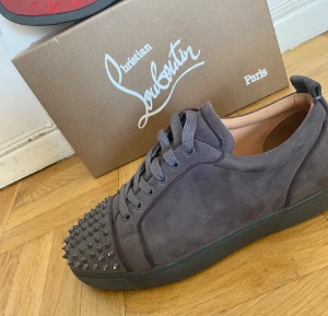 loubs - Mörkgrå sneakers från Christian Louboutin i mocka med coola nitar på tån. Klassisk låg modell med matchande grå sula och snörning. Snygg och edgy design som sticker ut med exklusiv känsla.