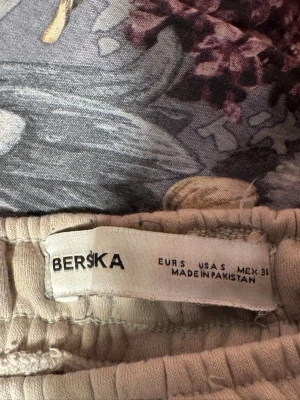 Beige mjukisbyxor från Bershka - Säljer ett par beige mjukisbyxor från Bershka med bred resår i midjan och raka ben. Byxorna har sidofickor och är tillverkade i ett mjukt och bekvämt material, perfekta för chill dagar. Klassisk och enkel design som passar till det mesta.