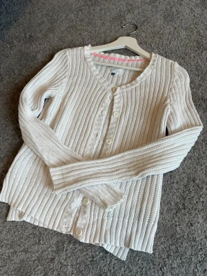 Vit ribbstickad kofta från H&M - Snygg vit ribbstickad kofta, rundhalsringning och knäppning framtill. Koftan har långa ärmar och är gjord i ett mjukt, stickat material. Kommer ej till användning.