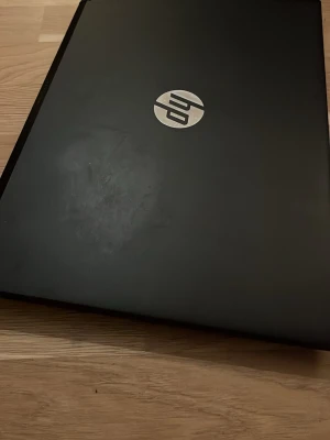 Svart HP bärbar dator - Säljer en stilren svart bärbar dator från HP med klassisk design. Datorn har ett fullstort tangentbord och HP-logga i silver på locket. Perfekt för studier, surf eller gaming. Materialet är matt plast och färgen är helsvart. Laddare följer med. Det är en repa i skärmen som man kan se på bilden därför priset