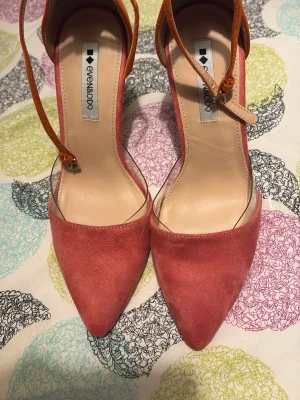 Rosa pumps med spetsig tå från Even&Odd - Snygga rosa pumps från Even&Odd med spetsig tå och smala orangea ankelremmar. Skorna har en elegant design och är tillverkade i mockaliknande material. Perfekta för att lyfta din outfit med en färgklick och stilren form. Aldrig använd.