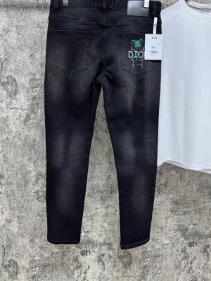 Svarta Dior jeans med björn-detalj - Säljer ett par svarta jeans från Dior med en unik grön björn-brodyr på bakfickan och klassisk femficksdesign. Jeansen har en snygg tvättad look och raka ben. Perfekta för dig som vill ha något extra i garderoben.