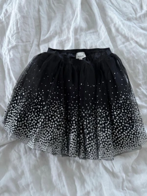 Svart glittrig kortkjol från KappAhl - Snygg svart kortkjol från KappAhl med glittriga paljettdetaljer. Kjolen har ett fluffigt tylltyg och resår i midjan för skön passform. Perfekt för dig som vill sticka ut med lite extra glitter eller till dig som ska på maskerad✨🖤