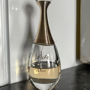 J'adore Eau de Parfum från Dior - J'adore Eau de Parfum från Dior i en elegant droppformad glasflaska med guldfärgad metallkork. Doften är lyxig och feminin, och flaskan har en exklusiv design som verkligen sticker ut på parfymhyllan.