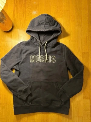 Mörkblå  hoodie från Morris🤩🙌 - Snygg svart hoodie från Morris med vit broderad logga på bröstet. Klassisk modell med huva och vita dragsnören samt en stor magficka framtill. Perfekt för en avslappnad och trendig stil.🙌