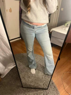 Ljusblå bootcut jeans - Säljer ett par ljusblå bootcut jeans med klassisk femficksdesign och normal midja. Jeansen har en lätt utsvängd passform nertill och stängs med dragkedja och knapp. Perfekta för en avslappnad och trendig look.