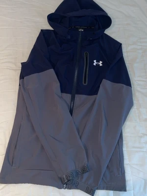 Under Armour vindjacka - Snygg vindjacka från Under Armour i mörkblått och grått. Jackan är i jätte bra skick. Storlek S kan även passa M. Pris kan diskuteras!