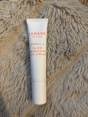 Lumene Nordic-C Glow Eye Cream - Fräsch ögonkräm från Lumene Nordic-C Glow Awakening Eye Cream i vit tub med orange text. Perfekt för att pigga upp huden runt ögonen och ge lyster. Smidig att ta med i väskan och enkel att applicera.