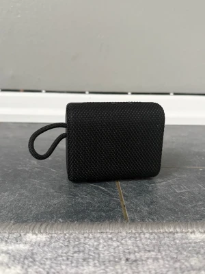JBL GO3 trådlös högtalare svart - Snygg och kompakt JBL GO3 trådlös högtalare i svart. Högtalaren har en robust design med tygmaterial runt om och gummidetaljer. Perfekt för att ta med sig överallt tack vare den smidiga storleken och den praktiska remmen.