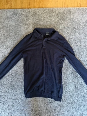 Mörkblå långärmad pikétröja Matinique - Snygg mörkblå långärmad pikétröja från Matinique med klassisk krage och tre knappar framtill. Tillverkad i mjukt material som passar perfekt till både jeans och chinos. Enkel och stilren design som funkar till många olika looks.