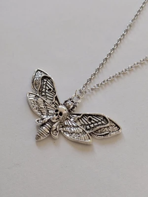 "Death Moth" eller "Silence of the Lambs moth" - Silvrigt halsband dödskallesvärmare (ofta kallad "Death Moth" eller "Silence of the Lambs moth"). Det är ett populärt motiv. En fjäril med sitt fascinerande dödskalleliknande teckningen på ryggen. Materialet rostfritt stål.