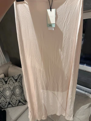 Krämvit långkjol från Gina Tricot - Lång, krämvit kjol från Gina Tricot i mjukt och tunt material. Kjolen har en enkel och rak design och är i storleken S. Aldrig använd med prislapp kvar. 