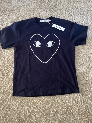 Mörkblå t-shirt Comme des Garçons Play - Mörkblå t-shirt från Comme des Garçons Play med det ikoniska hjärtmotivet med ögon på bröstet. Storlek M men passar bättre S