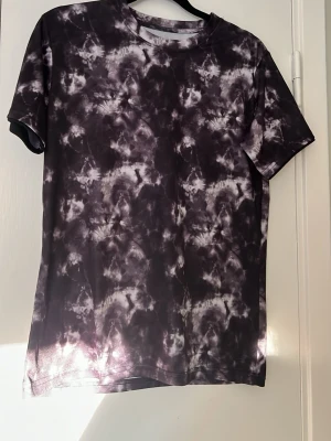 Svartvit tränigs t-shirt - Cool t-shirt med svart och vit tie dye-mönster. Klassisk passform med rund hals och korta ärmar. Perfekt för träning eller chill. Materialet känns mjukt och lätt, vilket gör den skön att ha på sig under aktiva dagar. Har egentligen 158/164 i storlek men är stor i storleken så fungerar jätte bra om man har xs/s i storlek.