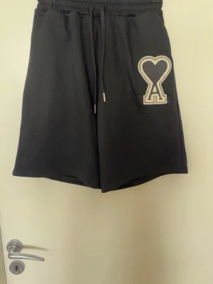 Svarta shorts med hjärtlogga Ami - Svarta shorts från Ami med elastisk midja och snörning. På vänster ben finns en stor vit hjärtformad Ami-logga. Shortsen har en avslappnad passform och är perfekta för en chill stil.