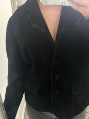 Svart kavaj med stora knappar - Snygg svart kavaj med klassisk krage och tre stora knappar framtill. Kavajen har två fickor med lock och är långärmad. Perfekt för en stilren look och passar till många olika outfits. Saknar en knapp som medföljer så enkelt att sy på igen. Säljer då jag har för många jackor