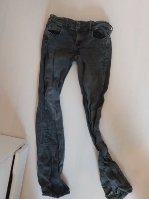 Mörkgrå slim fit jeans - Säljer ett par mörkgrå slim fit jeans med klassiska fem fickor och snygga detaljer på bakfickan. Jeansen har en låg midja och är tillverkade i ett stretchigt denim-material som sitter tight och bekvämt. Perfekt för dig som gillar en modern och stilren look.