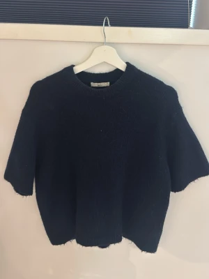 Svart stickad tröja Gina Tricot - Mysig svart stickad tröja från Gina Tricot med korta ärmar och rund hals. Tröjan har en fluffig struktur och är tillverkad i ett mjukt material som känns lyxigt. Perfekt för lager på lager och enkel att styla till olika outfits.