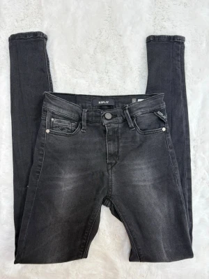 Svarta skinny jeans från Replay - Snygga svarta skinny jeans från Replay med diskreta slitningar och klassisk femficksdesign. Jeansen har hög midja, dragkedjegylf och silverfärgade nitar. Perfekta för en trendig och avslappnad look.