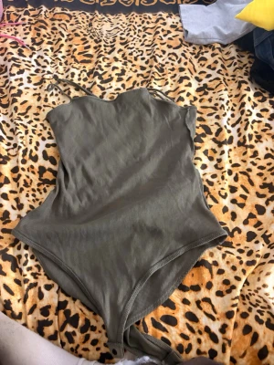 Olivgrön ribbad body med smala axelband - Snygg olivgrön body i ribbat tyg med smala axelband och rundad halsringning. Materialet ser stretchigt och bekvämt ut, perfekt för att styla med jeans eller kjol. Inga synliga märken på plagget.