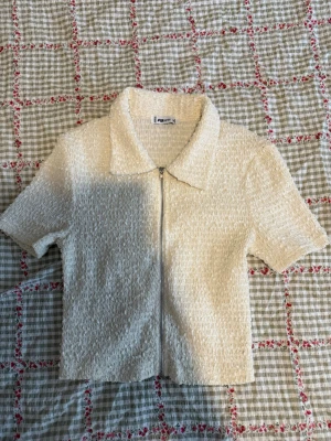 Krämvit kortärmad topp från New yorker  - Superfin krämvit topp från New Yorker med korta ärmar, krage och dragkedja framtill. Materialet är strukturerat och ger en cool textur. 