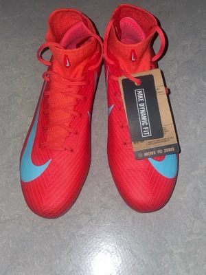 Nike Mercurial rosa/oranga fotbollsskor - Snygga Nike Mercurial fotbollsskor i en stark rosa färg med ljusblå detaljer och Dynamic Fit-krage. Skorna har snörning, syntetiskt material och mönstrad sula för bra grepp på planen. Perfekta för dig som vill sticka ut på fotbollsplanen. Jag säljer dessa eftersom jag fick de som present men de passar inte mig alls, aldrig använt de alltså de är helt sprillans nya 