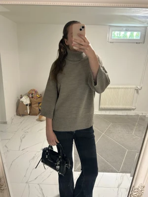 Beige stickad polotröja - Säljer en beige stickad polotröja med breda trekvartsärmar och ribbade detaljer vid ärmslut och nederkant. Tröjan har en hög, mysig polokrage och en avslappnad passform som är perfekt för lager-på-lager-stil.