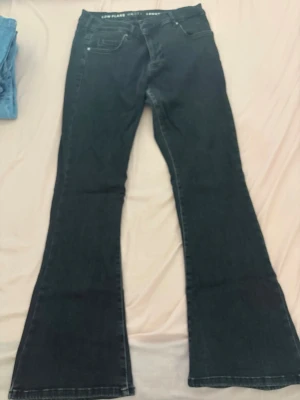 Svarta bootcut jeans low flare - Säljer ett par svarta bootcut jeans med låg midja och flare-ben. Klassisk femficksmodell och knappgylf. Jeansen har en enkel, stilren look och passar perfekt till sneakers eller boots. Materialet är denim med lite stretch för extra komfort.